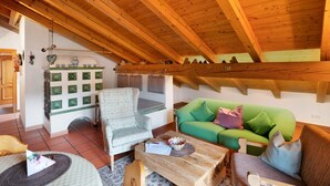 A cozy room with a wooden ceiling, a green sofa, a patterned armchair, and a wooden coffee table. - Apartment 'Edelweiß Nr 5' with Mountain View, Shared Garden and Wi-Fi (Mittenwald)