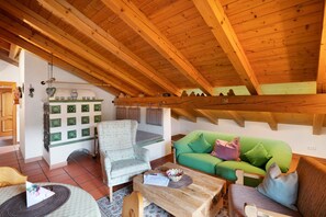 Une pièce chaleureuse avec un plafond en bois, un canapé vert, un fauteuil à motifs et une table basse en bois.
