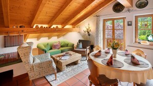 A cozy living room with wooden beams, a green sofa, patterned chairs, a coffee table, and a dining table set for four. - Apartment 'Edelweiß Nr 5' with Mountain View, Shared Garden and Wi-Fi (Mittenwald)