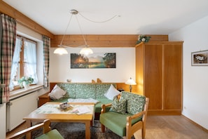 Una habitación acogedora con techo de madera, un conjunto de sofá verde, una mesa de madera y un ventanal con cortinas.