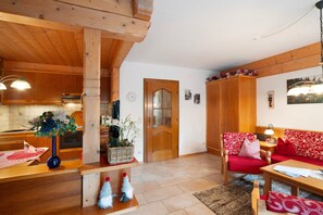 A wooden interior with a kitchen, a wooden door, a red sofa, and a table with a lamp.