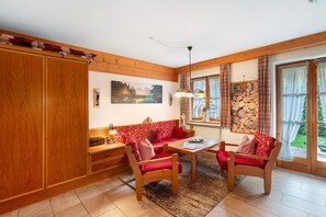 Um quarto acolhedor com um banco de madeira, uma mesa e um sofá. Há um quadro na parede e uma janela com cortinas.