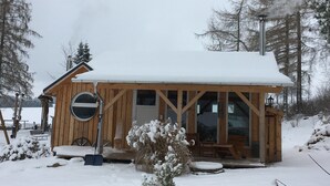 Une cabane en bois avec un toit enneigé, une cheminée et une terrasse dotée de bancs.