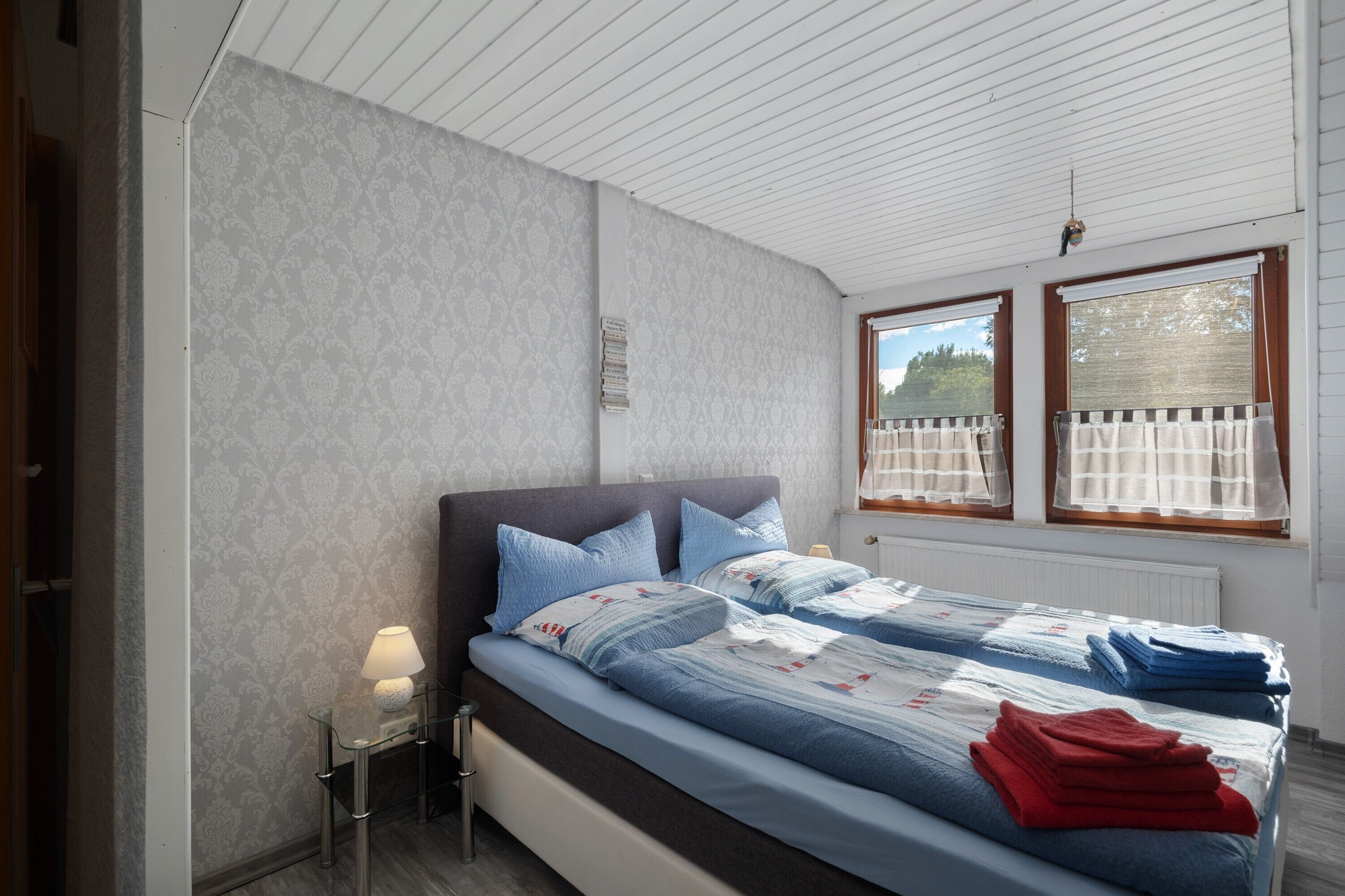 Une chambre à coucher avec un lit, une table de chevet, une lampe et des fenêtres avec des rideaux.