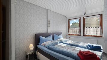Une chambre à coucher avec un lit, une table de chevet, une lampe et des fenêtres avec des rideaux.
