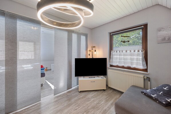 A modern room with a flat-screen TV, a sofa, a window with a view, and a ceiling light fixture.
