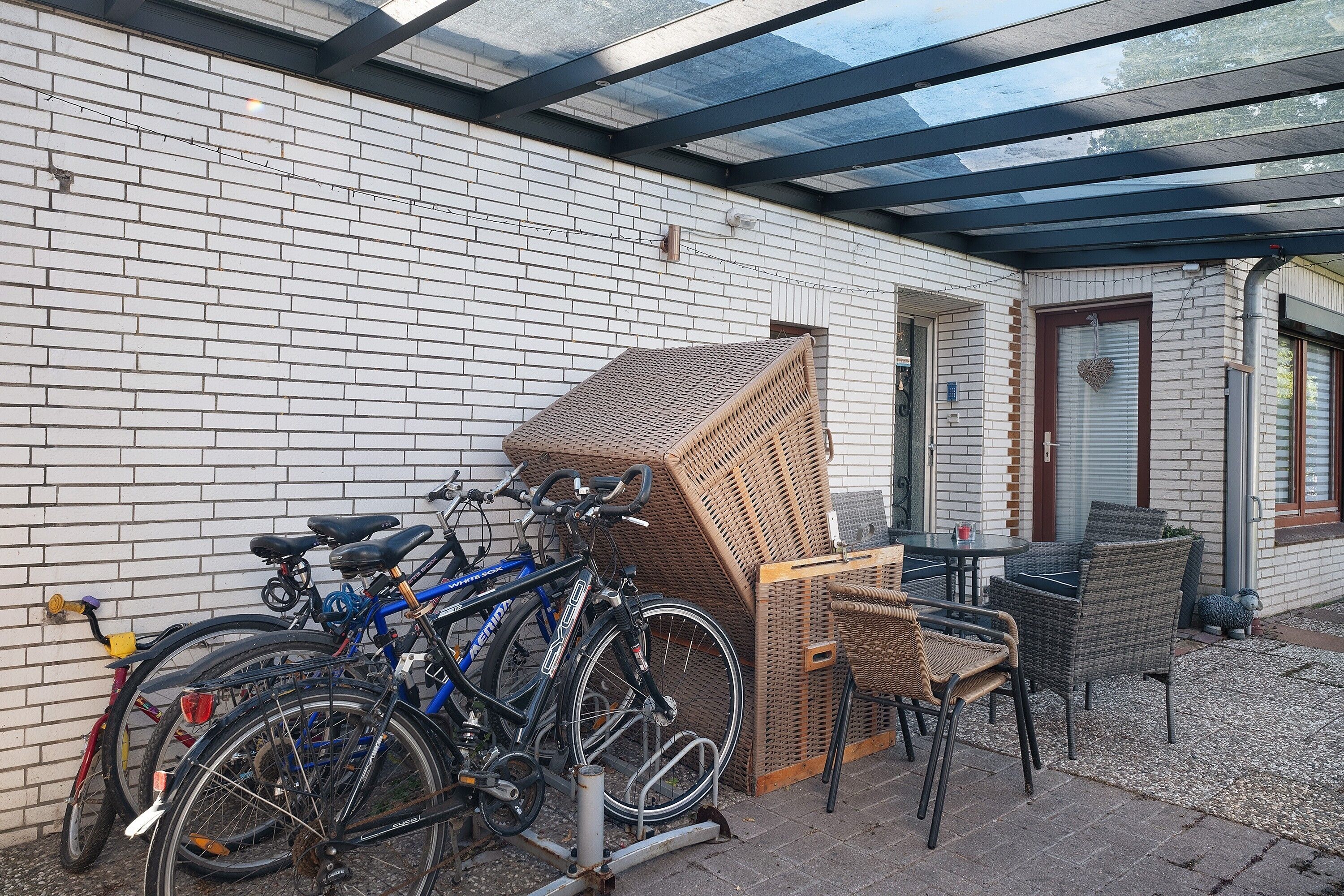 Un espace extérieur abrité, doté d’un mur en briques, de vélos, de meubles en osier et d’un toit en verre.