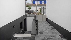 Une ruelle étroite avec un petit espace aménagé pour s’asseoir, un escalier et une vue sur un bâtiment en arrière-plan.