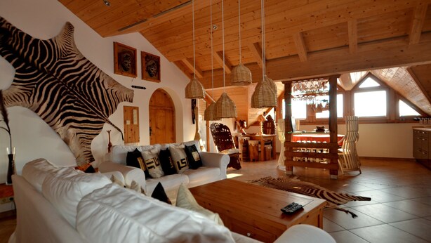 A spacious living room with a large sofa, wooden ceiling, and a zebra rug.