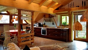 A spacious kitchen with wooden beams, a dining area with chairs, and a large window.
