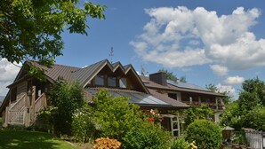 A large house with a sloped roof, a wooden staircase, and a garden with various plants and flowers.