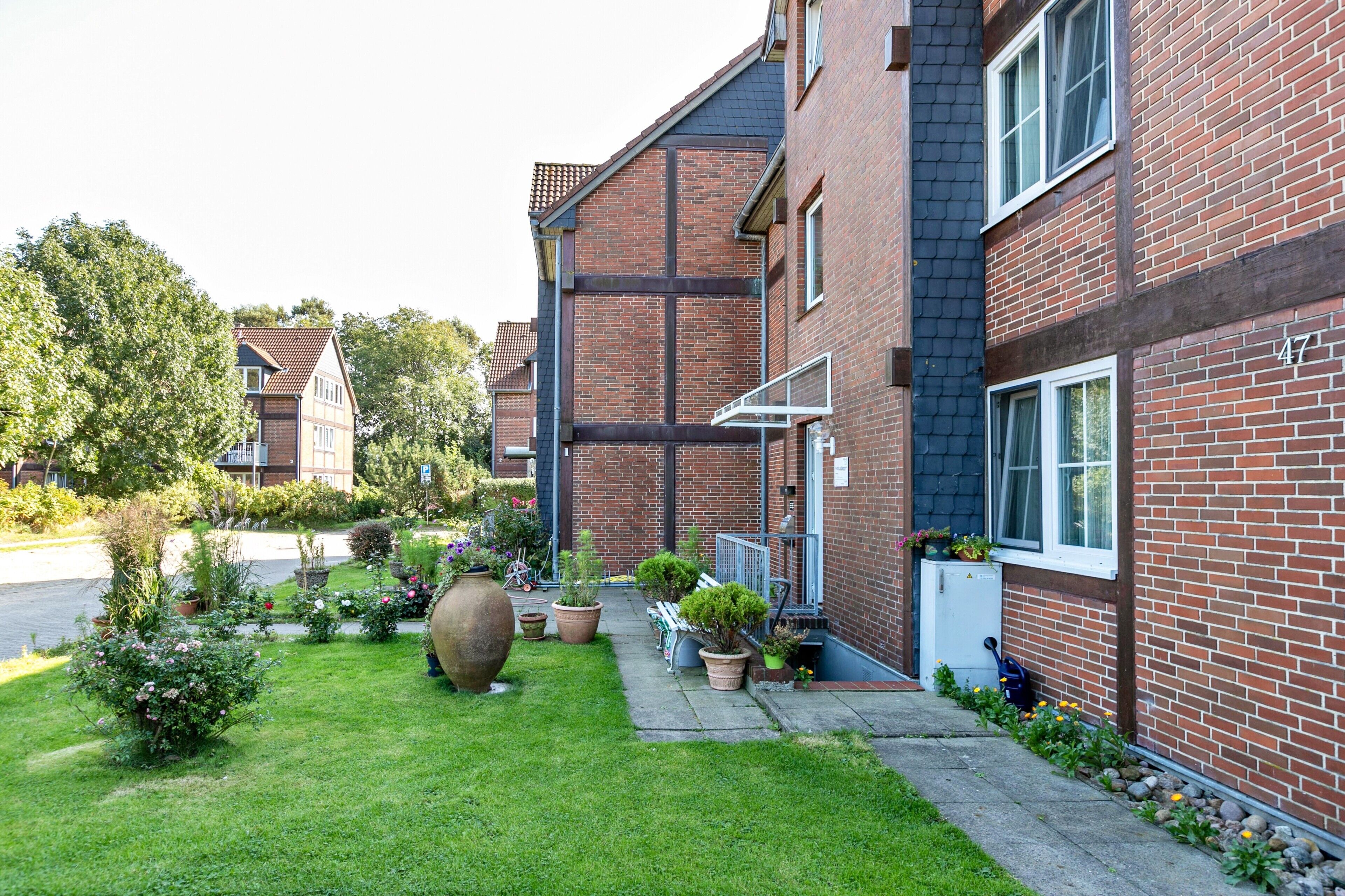 A residential building with a brick facade, a well-maintained lawn, and potted plants.