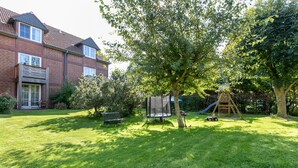 Patio trasero residencial con un trampolín, un tobogán, una casita de juegos de madera y una casa de ladrillo.