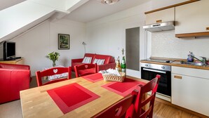 Una cocina moderna con horno empotrado, un comedor con sillas rojas y una mesa de madera, y un sofá rojo en la sala.