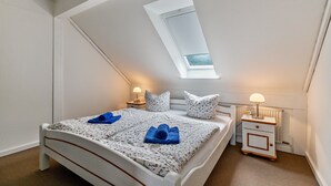 Un dormitorio con techo inclinado, tragaluz, cama con ropa de cama floral, dos mesitas de noche con lámparas y un radiador.