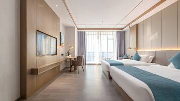 A hotel room with a large bed, a desk with a chair, a television, and a window with curtains.