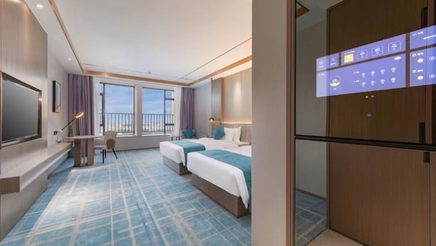 A hotel room with two beds, a desk, a TV, and a balcony.