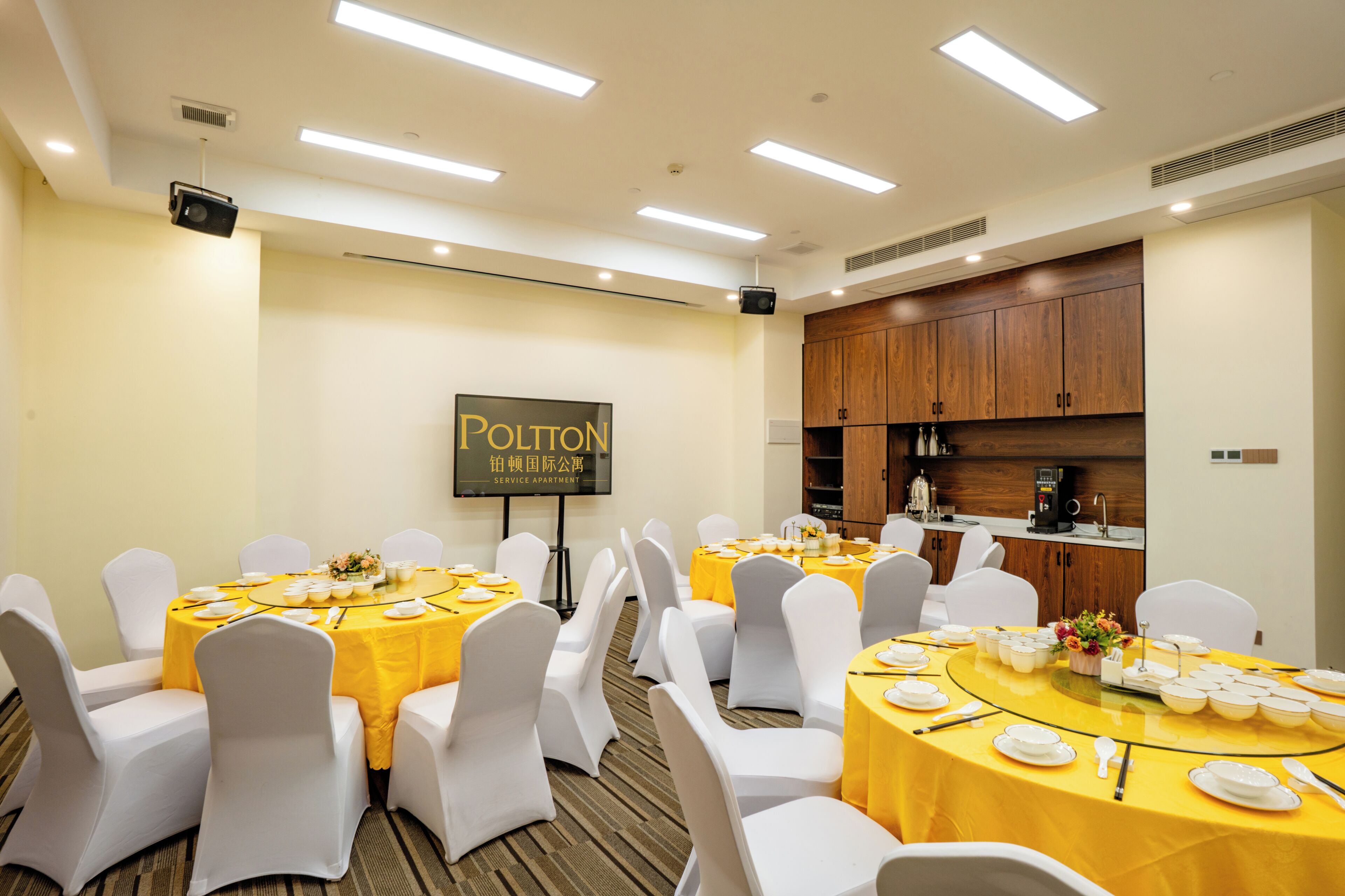 A conference room with round tables, white chairs, and a service apartment sign on the wall.