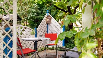 En patio med hvidt espalier, et lille bord med rød pude og en rød stol.