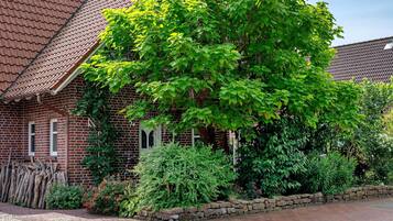 Ein Haus aus Backsteinen mit einem Ziegeldach, ein großer Baum davor und eine Steinmauer.