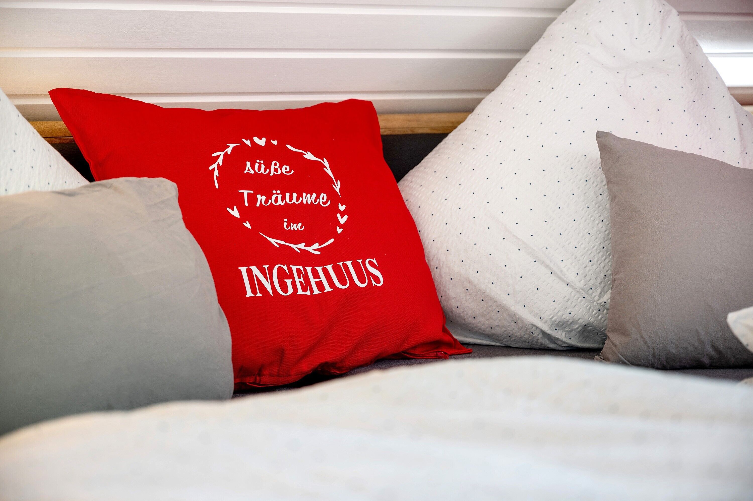 Un lit avec des oreillers, dont un rouge avec du texte et d’autres dans des tons neutres.