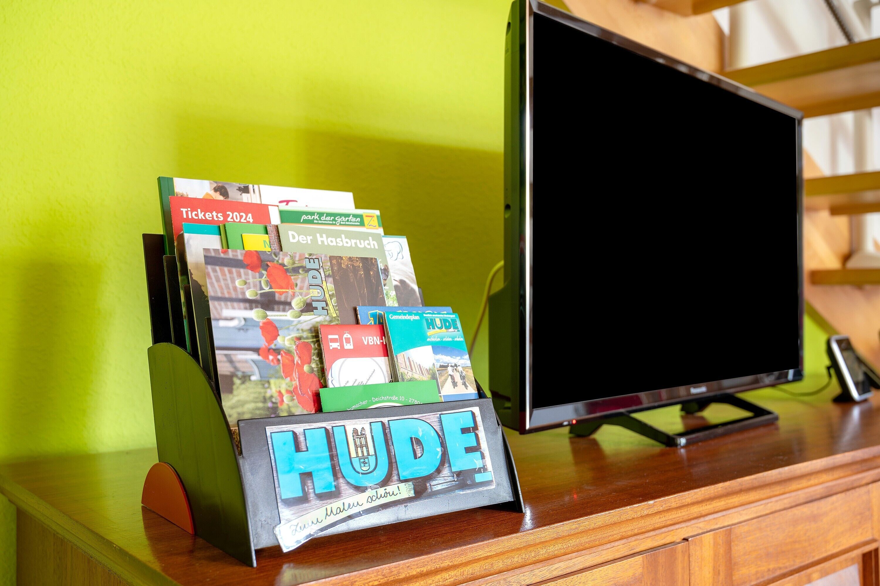 A desk with a magazine rack displaying various travel and event brochures, a television, and a telephone.