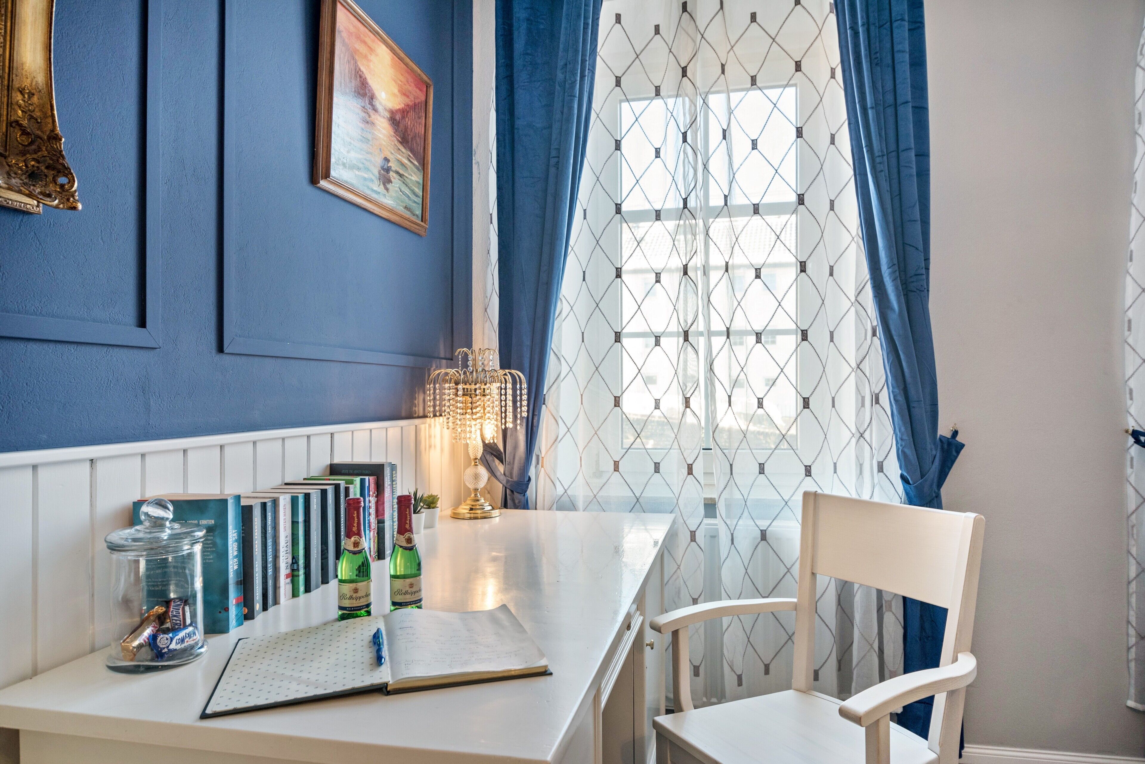 Una habitación con una mesa blanca, libros, un tarro de vidrio, una botella y una silla.