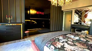 Una habitación de hotel moderna con una cama grande, un televisor, un minibar y un espejo.