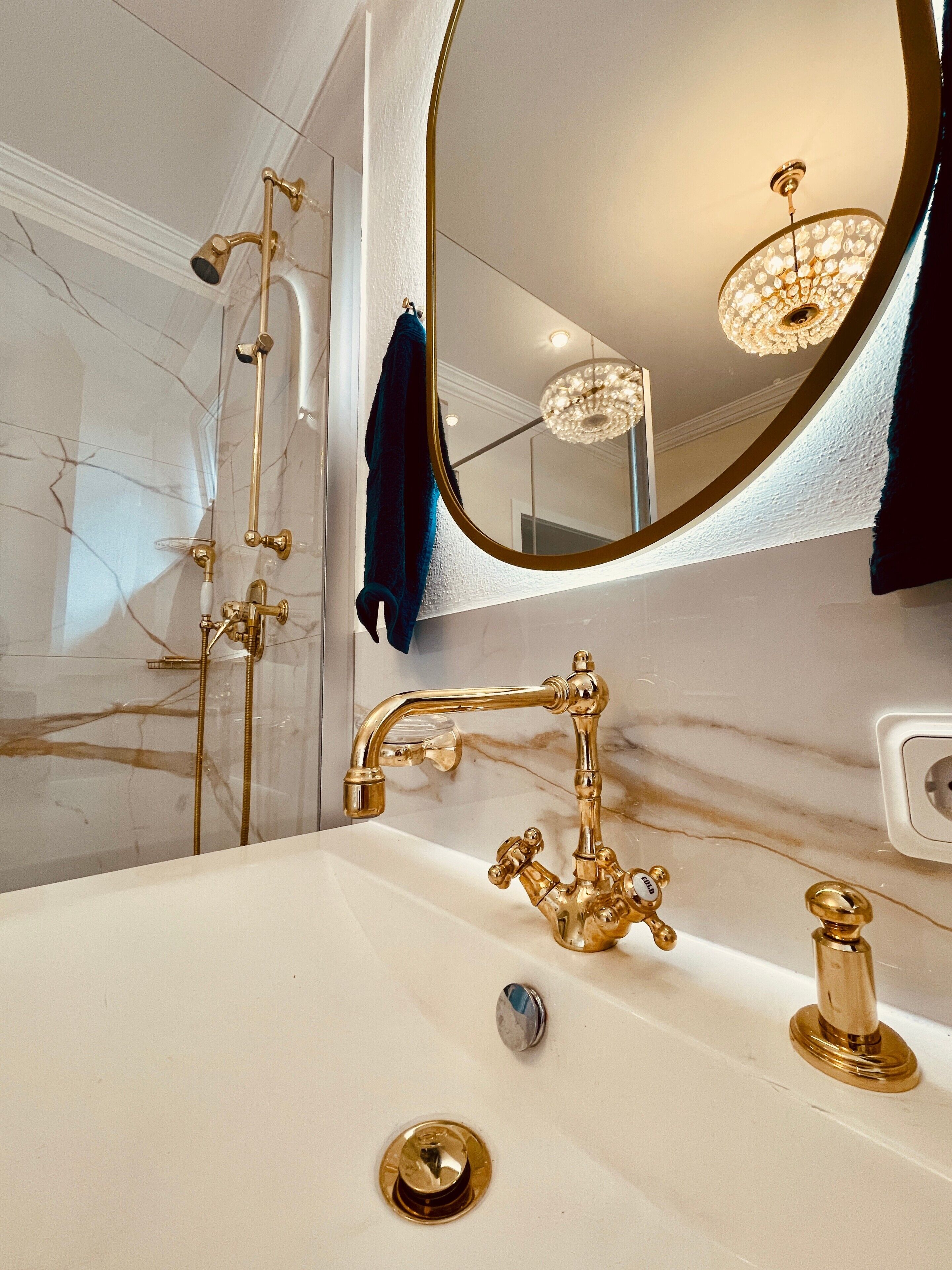 A bathroom with a gold faucet, a round mirror, and a chandelier.