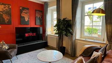 A living room with a TV, red walls, a globe artwork, a plant, and a view of the outside.