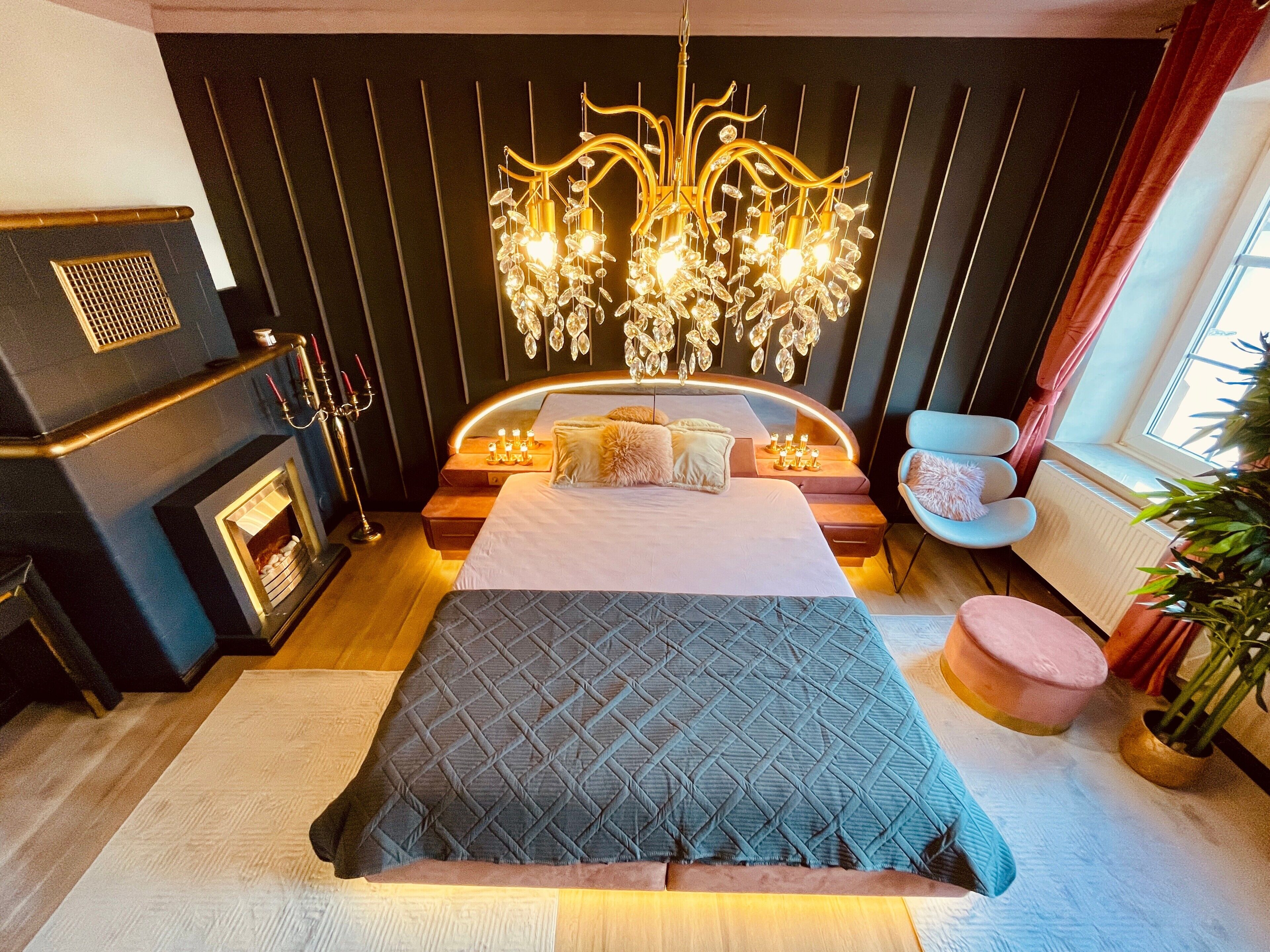Een moderne slaapkamer met een groot bed, een kroonluchter, een open haard en een raam met gordijnen.