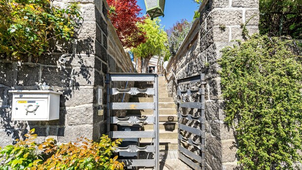 A narrow stone pathway leading to a gate with a metal fence, surrounded by greenery and a clear blue sky. - Carpe Diem Apartment with Shared Garden and Wi-Fi (Görlitz)