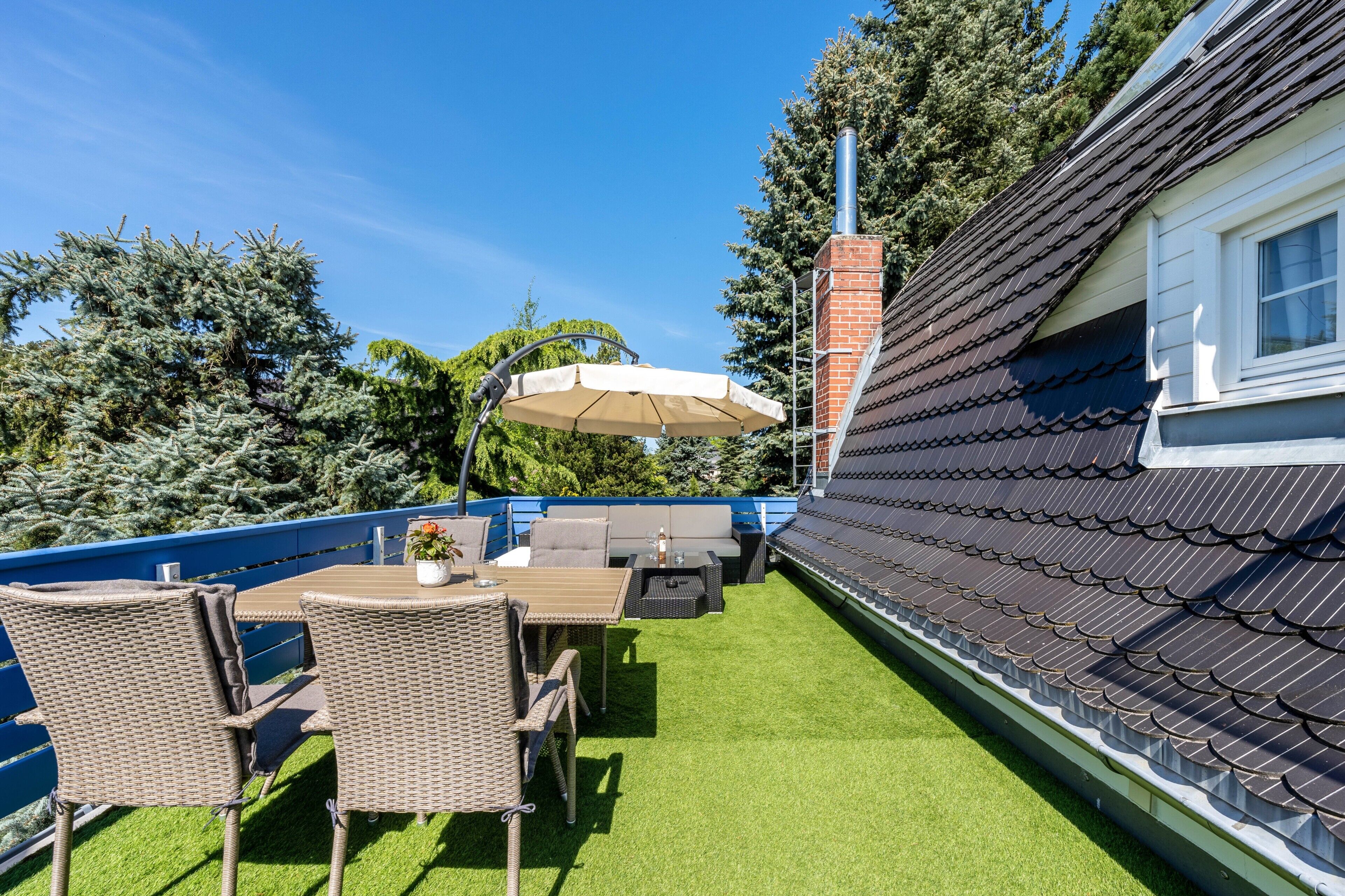 Terraza en la azotea con mobiliario exterior, una parrilla y vistas a los árboles circundantes.