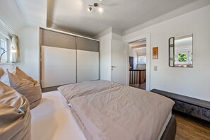 Une chambre à coucher comprenant un lit, une armoire, un banc, un miroir et une porte donnant sur une salle de bain.