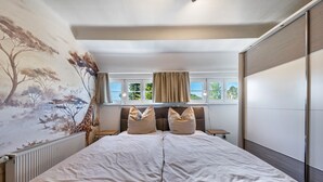 A bedroom with a large bed, a mural on the wall, a window with curtains, and a radiator. - Carpe Diem Apartment with Shared Garden and Wi-Fi (Görlitz)