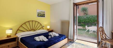 A room with a bed, a nightstand, a lamp, a chair, and a view of the outside.