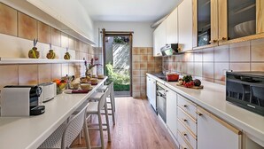 A modern kitchen with white cabinets, a built-in oven, and a large window. - Il Giardino di Riva - Garden Apartment Near the Lake (Riva del Garda)
