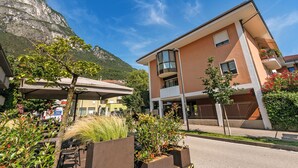 A modern building with a balcony, surrounded by greenery and a mountain backdrop. - Il Giardino di Riva - Garden Apartment Near the Lake (Riva del Garda)