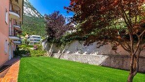 A well-maintained lawn, a stone wall, and a building with balconies. - Il Giardino di Riva - Garden Apartment Near the Lake (Riva del Garda)
