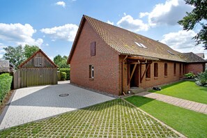 Een gebouw van baksteen met een schuin dak, een houten deur en een verharde oprit.