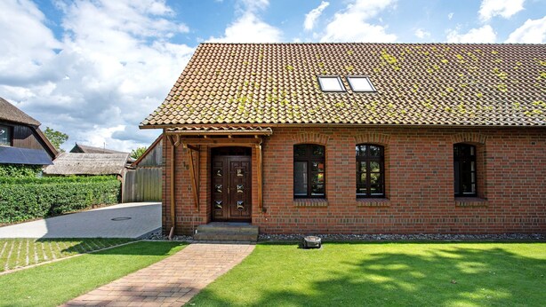 Une maison en briques avec un toit en tuiles, une porte en bois et une allée pavée.