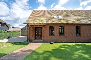Une maison en briques avec un toit en tuiles, une porte en bois et une allée pavée.