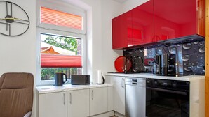 Une cuisine compacte avec des meubles blancs, un meuble supérieur rouge, un four encastré et une machine à café.