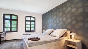 Une chambre à coucher avec un lit en bois, deux fenêtres, une table de chevet et une lampe.