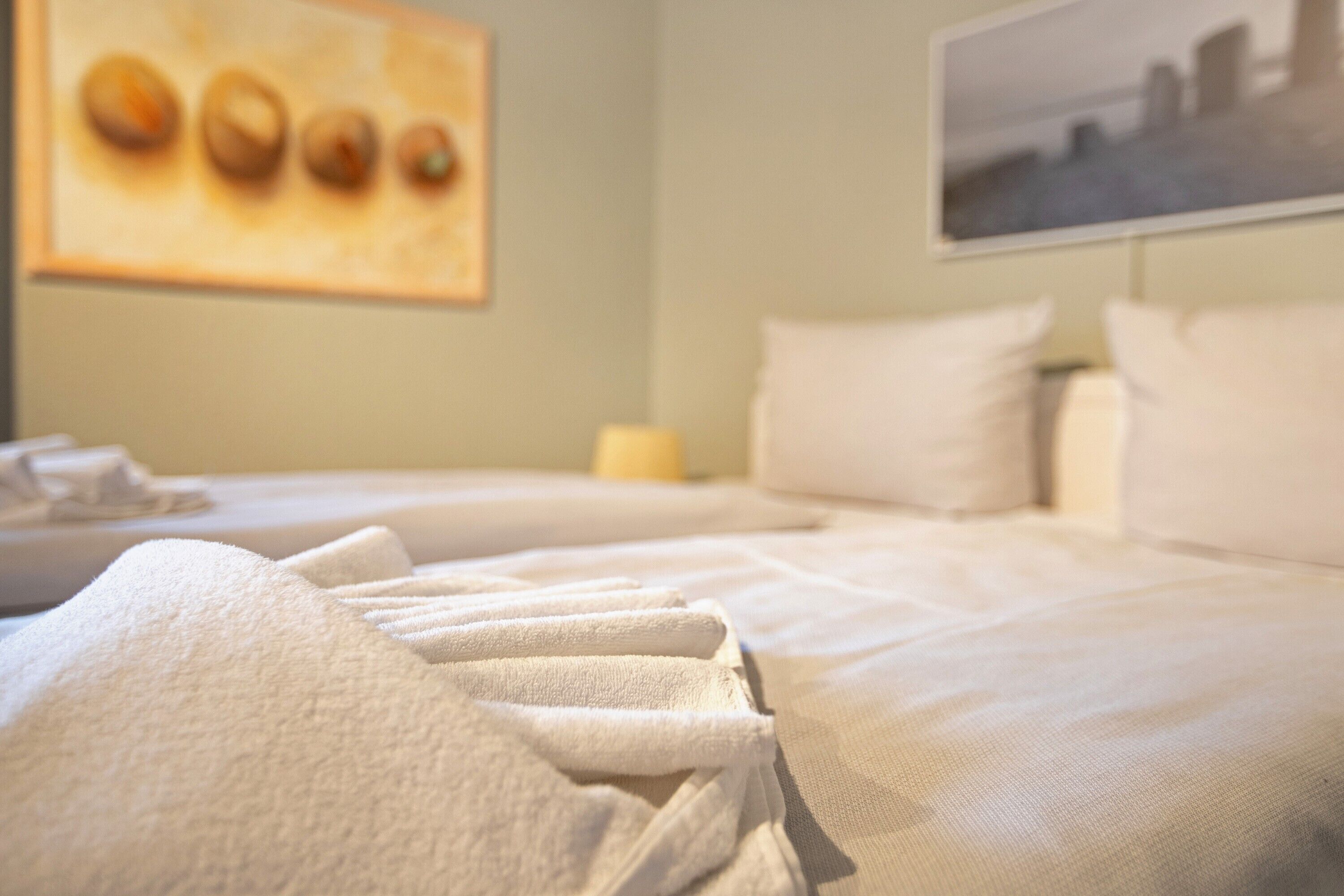 A hotel room with a neatly made bed, a painting on the wall, and a window with a view.