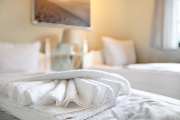 A neatly made bed with white linens, a bedside table with a lamp, and a painting on the wall.