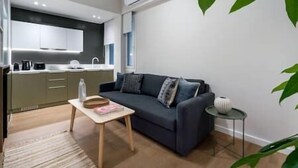 Un salon moderne avec un canapé bleu foncé, une petite table en bois et un coin cuisine à l’arrière-plan.