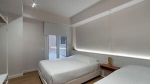 Une chambre moderne avec deux lits, une petite table de chevet et une grande fenêtre.