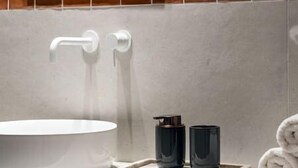 Une salle de bain avec un lavabo blanc, une serviette et deux récipients noirs posés sur un plateau en marbre.