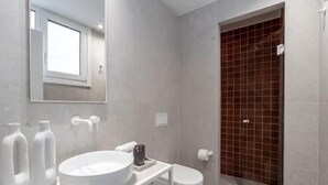 A modern bathroom with a large white sink, a toilet, and a shower area with brown tiles. - Central Bliss Suite D1 (Athens)